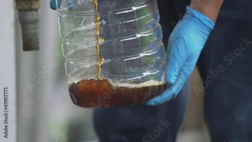 hand of man in blue rubber gloves opens a tap filling refined biodiesel into a clear plastic water tank. photo