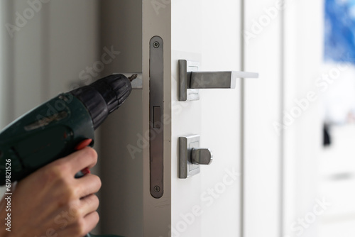 A locksmith is repairing an interior door lock. Close-up of male hands repairing or replacing an entrance door lock with a hex screwdriver