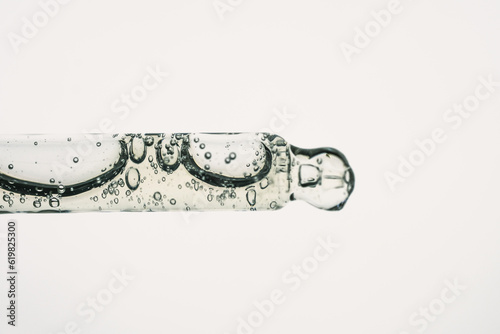 Glass pipette with cosmetic liquid or polyglutamic acid with air bubbles on white background. Side view, macro.