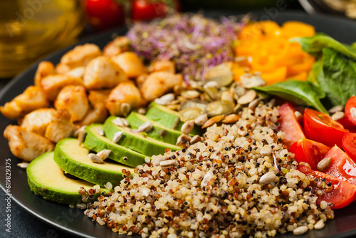 Salad with quinoa  avocado and chicken. Front view. Served on a black plate.
