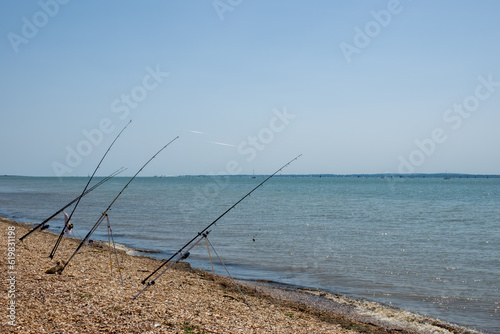 fishing rods in a row on a deserted beach with the sea and blue sky in the background © Penny