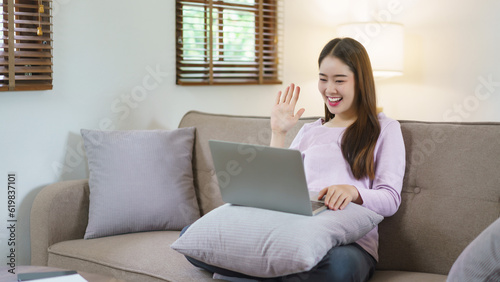 Women sitting on big sofa and greeting with friends in video call on laptop in lifestyle at home