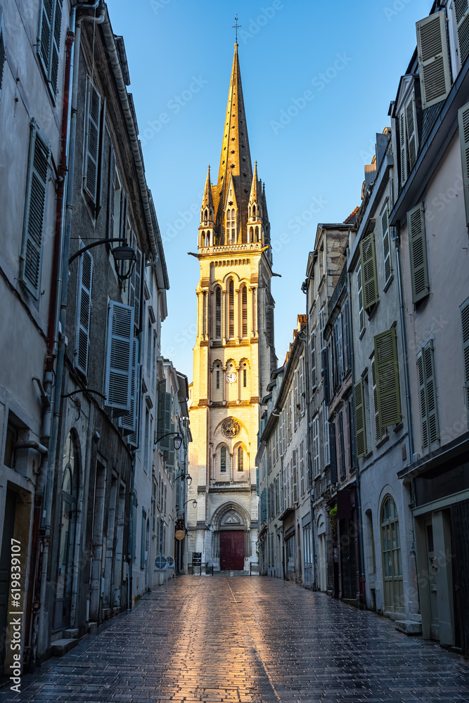 Narrow alley with picturesque streets and old church in the background illuminated by the sun, Pau, France.