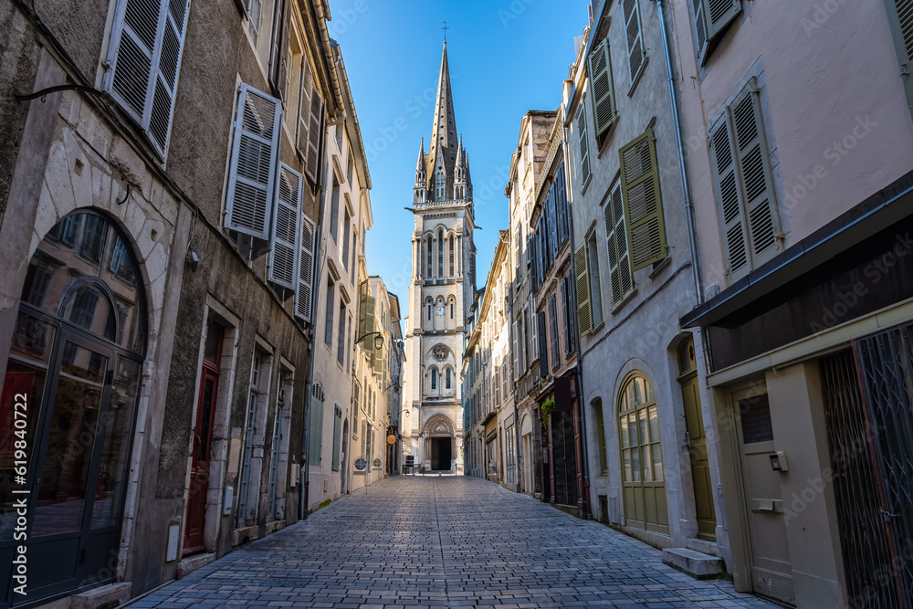 Narrow alley with picturesque streets and old church in the background illuminated by the sun, Pau, France.