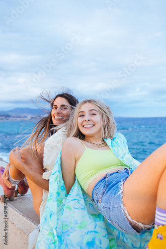Two young women, friends have fun and enjoy riding rollerblades on beach promenade. Funny, exciting fitness activity, train dancing moves, authentic laugh and real emotions of happiness  © BublikHaus