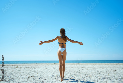 Tranquil beauty of secluded island getaway. Gorgeous sunkissed woman standing on the beach with open arms  blissful relaxation and harmony with nature