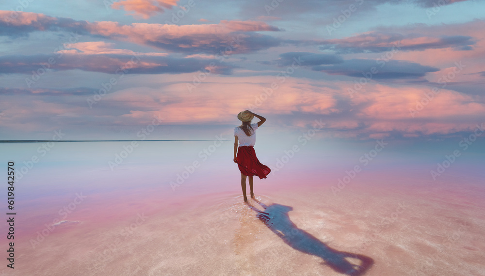 Rear view woman standing in beautiful pink lake with evening purple violet sunset sky, enjoying perfect landscap