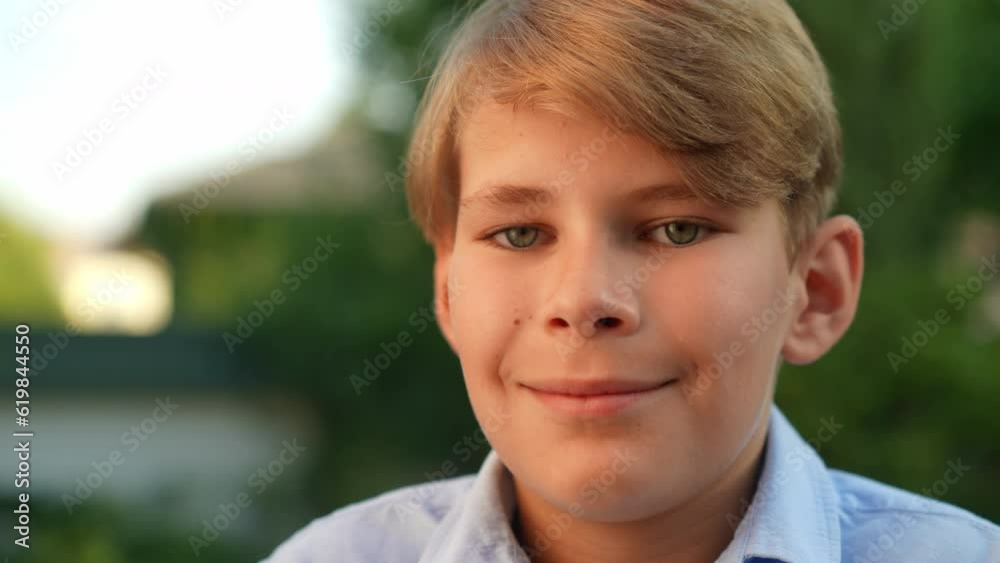 Headshot of happy blond boy with gray eyes looking at camera smiling. Relaxed happy Caucasian kid posing in slow motion in summer park outdoors Headshot of happy blond boy with gray eyes looking at camera smiling. Relaxed happy Caucasian kid posing in slow motion in summer park outdoors