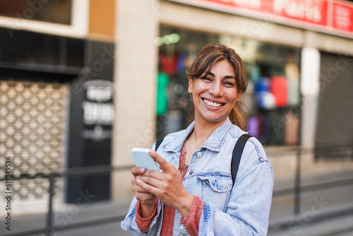 Quadro su tela Mature latin woman using mobile phone in the city while smiling on camera - Trav