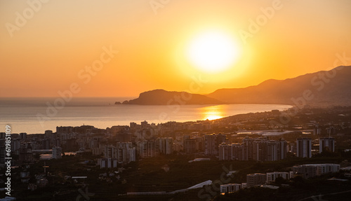 Beautiful sunset over the mediterranean sea and the city of Alanya in Turkey. The sunset is reflected in the water and slightly illuminating the city. Beautiful landscape.