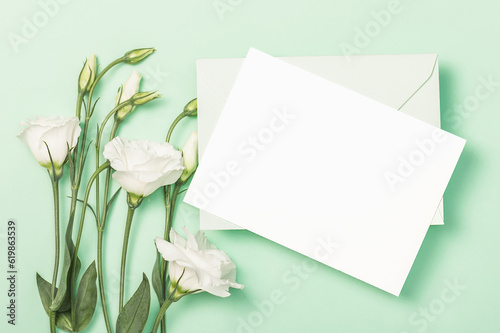Delicate white eustoma flowers, green envelope and empty card on green background. Flat composition.Greeting card, invitation.