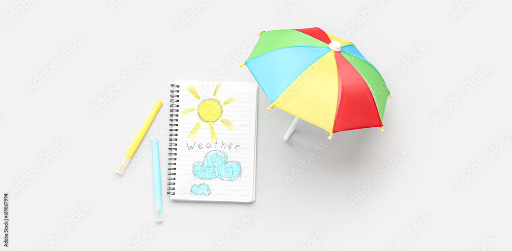 Notebook with drawings and small umbrella on light background. Weather forecast concept