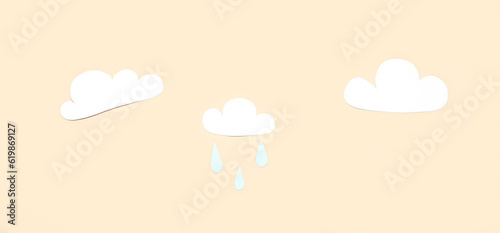 Paper clouds with rain drops on beige background. Weather forecast concept