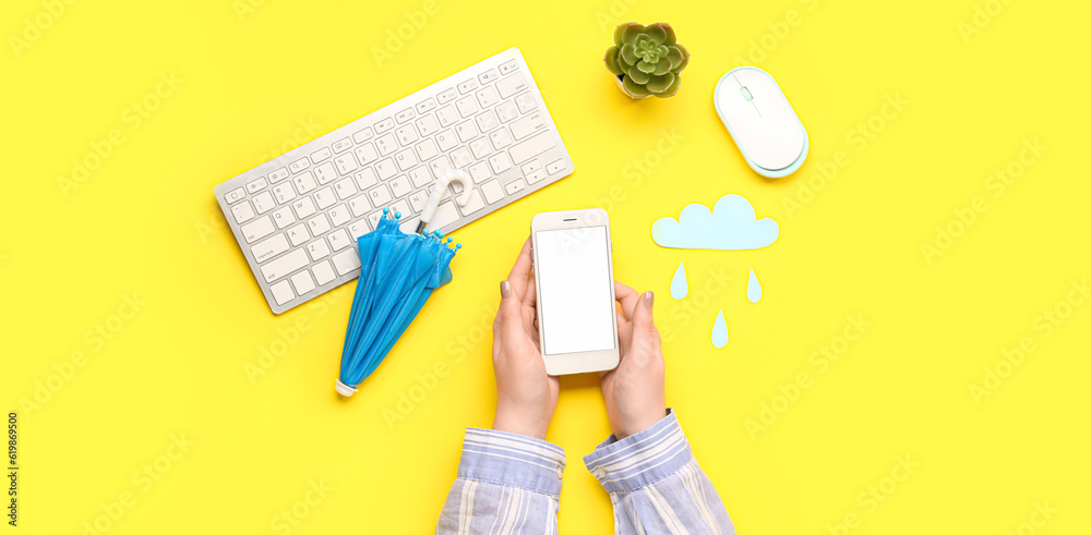 Female hands holding mobile phone, small umbrella, paper cloud and computer keyboard on yellow background. Weather forecast concept Female hands holding mobile phone, small umbrella, paper cloud and computer keyboard on yellow background. Weather forecast concept