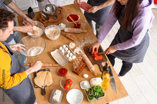 Group of young people with chef preparing Italian pizza during cooking class in kitchen