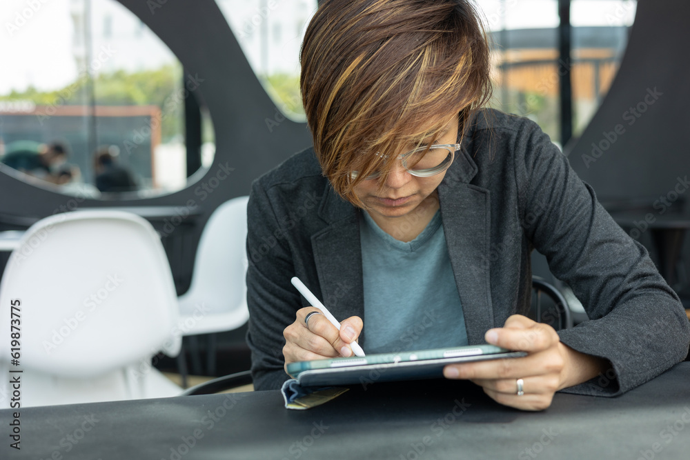 Step into the modern world of digital creativity with a young, smart Asian woman as she navigates her online workplace for her freelance work, using applications, touchpad, and wireless communication.