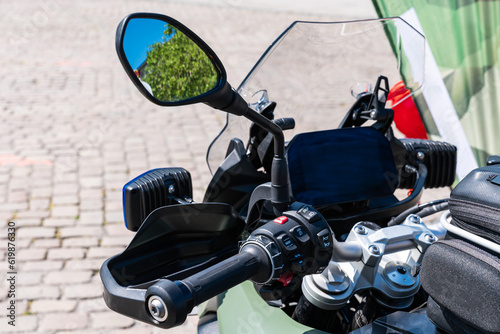 Part of a motorcycle steering wheel with various shift buttons and a rear view mirror. Close up.