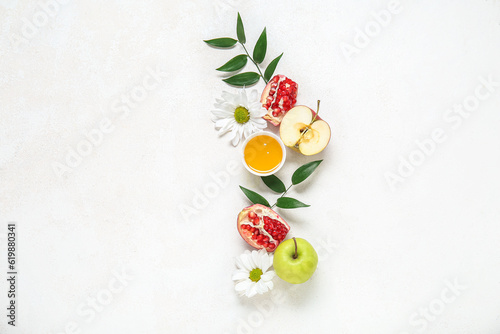 Composition with bowl of honey, ripe fruits, flowers and plant leaves on light background. Rosh hashanah (Jewish New Year) celebration
