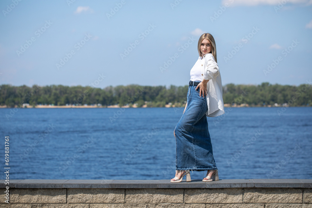 Portrait of a young beautiful blonde girl in long blue jeans skirt