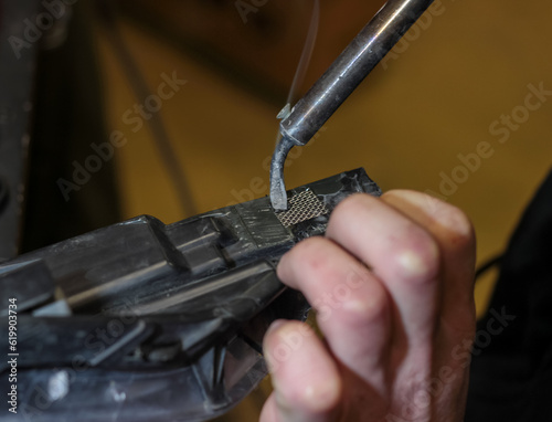 A man restores the plastic of the car body. The man has a soldering iron in his hands, with which he solders the parts. The mechanic repairs the car with a soldering iron.