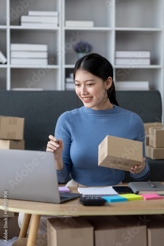 Asian woman online store business owner, online shop owner working from home, posting products for sale on website and accepting orders and packing products for customers with private courier service.