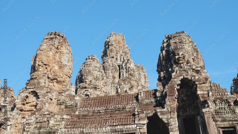 Image of the ancient Bayon Temple on a sunny day, displaying stone towers with human faces, located in Cambodia.