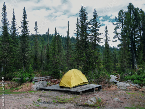 Tent camping in the taiga, a single tent on a wooden pedestal in the evening. Bad weather on a hike, camping in the rain. Camping life concept.