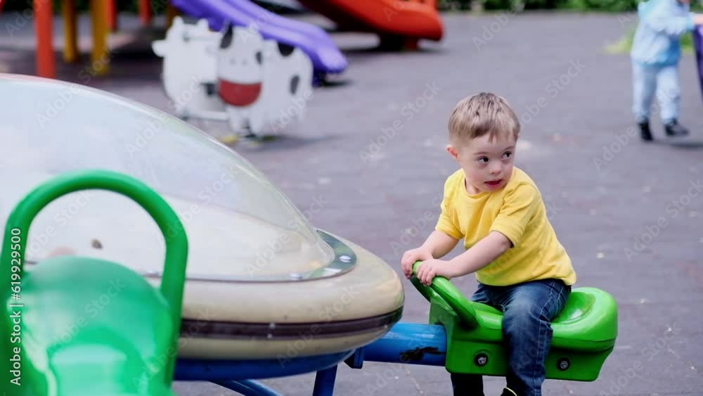 Cute little boy with Down syndrome trying modern playground seesaw equipment on summer day blond preschooler enjoying fun outdoor activity on walk with parents Cute little boy with Down syndrome trying modern playground seesaw equipment on summer day blond preschooler enjoying fun outdoor activity on walk with parents