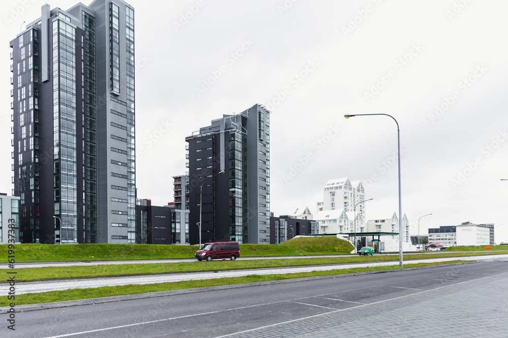vue sur une route avec une voiture rouge et des tour d'habitation en arrière plan lors d'une journée grise