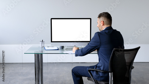 Businessman in formal suit sitting at table in front of computer with blank screen, mockup for business website design