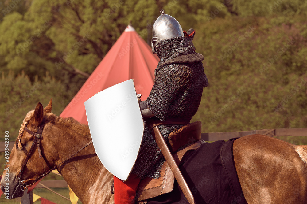 Medieval knight on a horse with a sword and shield. A man in chain mail with a weapon on horseback guards the border of the state