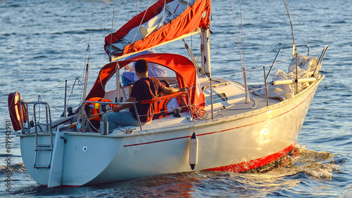 Fotografiet A company of people is sailing on a small sailboat on the sea at sunset, close-up