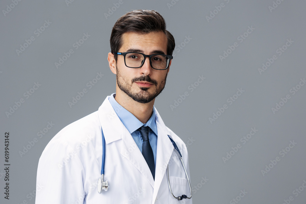 Fototapeta premium A serious doctor man in a white coat and eyeglasses and a stethoscope looks at the camera on a gray isolated background, copy space, space for text, health