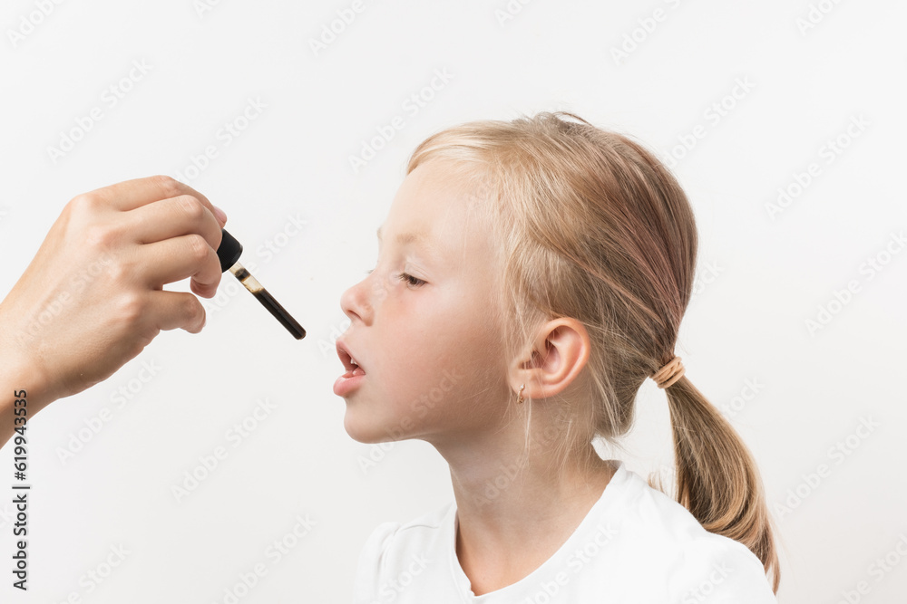 Portrait of happy cute caucasian girl taking supplement or medicine syrup in pipette on white background. Fever reducing treatment for children. Mild sedative for little kids. High temperature cure Portrait of happy cute caucasian girl taking supplement or medicine syrup in pipette on white background. Fever reducing treatment for children. Mild sedative for little kids. High temperature cure