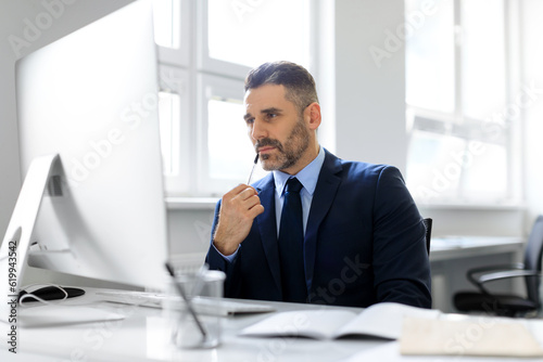 Thoughtful middle aged businessman working on computer sitting in office, thinking about new business project or startup
