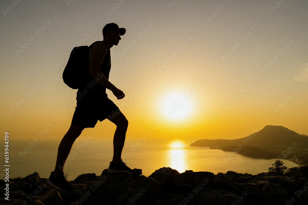 Silhouette of a man walking on the rocks of the mountains while hiking at sunset