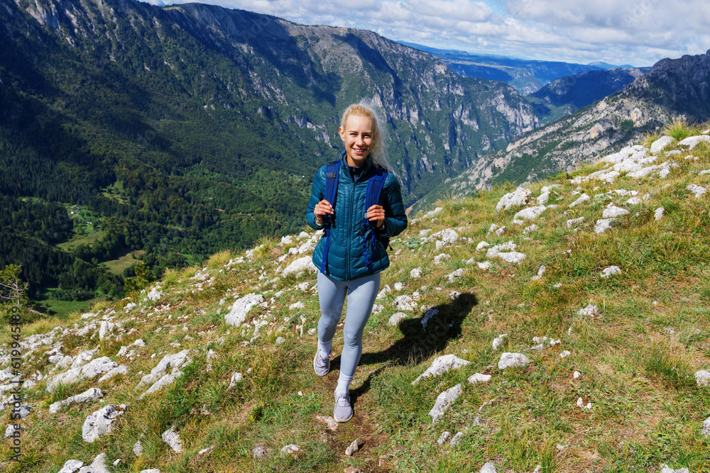 Active recreation in the mountains. A young woman with a backpack is walking along a mountain trail. Sunny weather