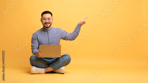 Online Offer. Smiling asian man with laptop pointing at copy space