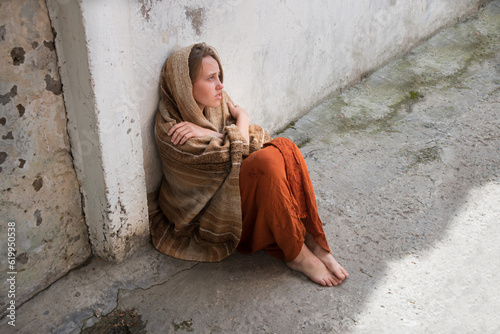 Fotografie A girl in poor clothes sits on the ground