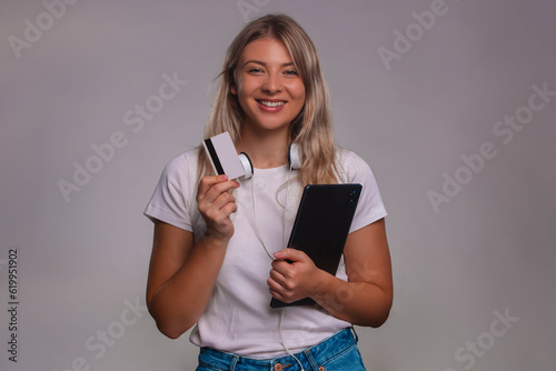 Young woman holding credit card and using tablet isolated on a gray background