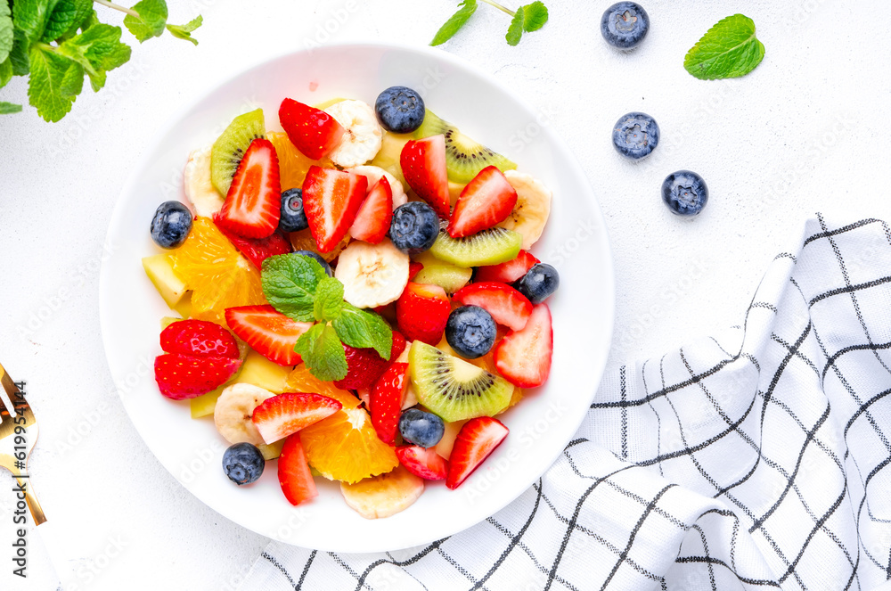 Fruit and berry salad with fresh strawberries, blueberries, banana, kiwi, orange and mint leaves, white table background, top view Fruit and berry salad with fresh strawberries, blueberries, banana, kiwi, orange and mint leaves, white table background, top view