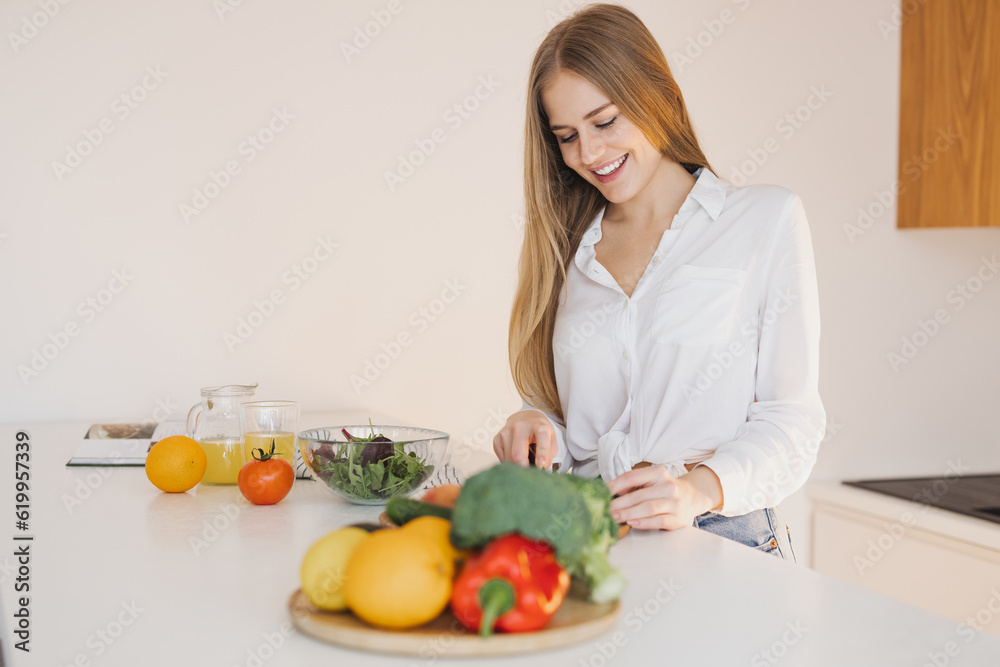 A happy cute blonde woman is preparing a salad in the kitchen A happy cute blonde woman is preparing a salad in the kitchen