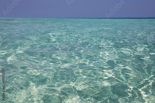 Emerald water texture, transparent sea surface with waves and sandy bottom. Turquoise color, natural background