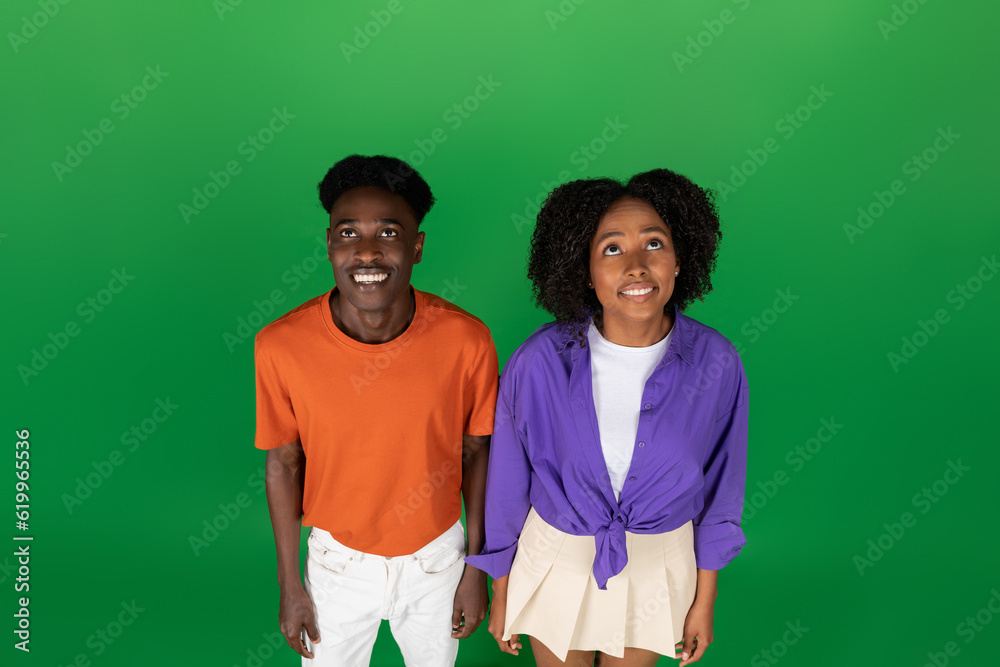 Smiling young african american guy and woman in casual looking up, isolated on green studio background Smiling young african american guy and woman in casual looking up, isolated on green studio background