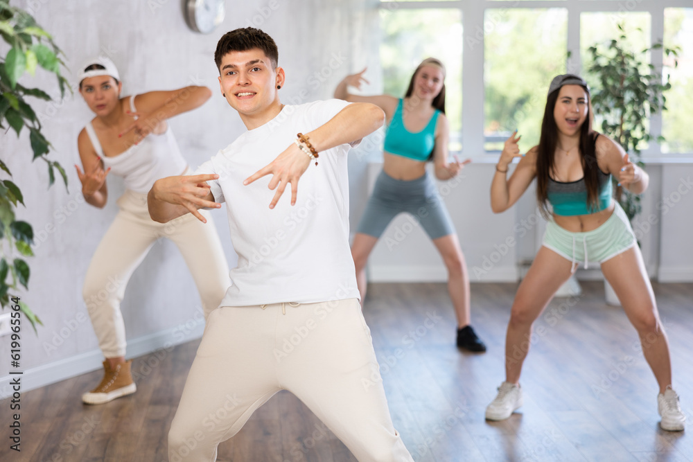 Fototapeta premium Group of young women and young guy perform hip hop dance moves in dance hall