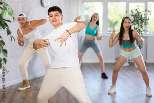 Group of young women and young guy perform hip hop dance moves in dance hall