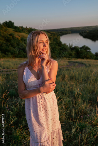 Pensive young woman on nature background in summer at sunset. female is relaxing in the field with flowers. Soft golden color