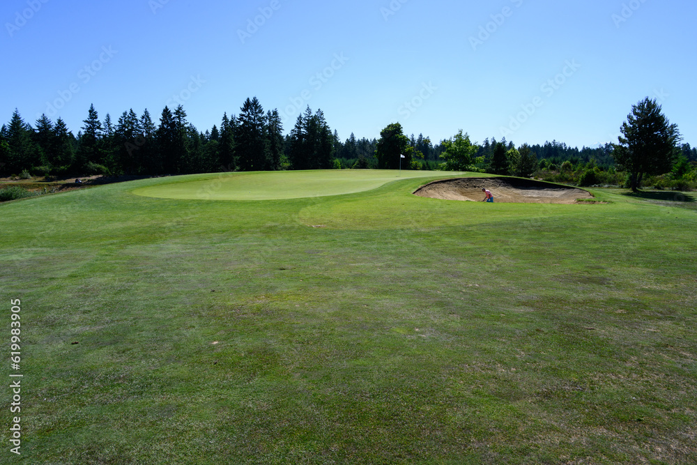 Relaxing day on the golf course, sand trap protecting the green with a white flag, person in the bunker
