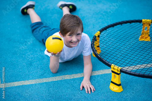 child playing sports game spikeball, spikeball. the boy is hitting the yellow ball in a miniature volleyball analog outside. photo