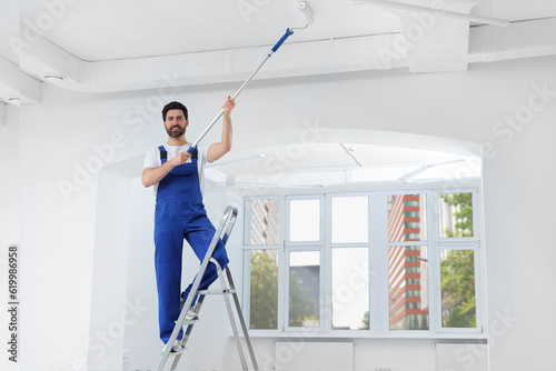 Handyman painting ceiling with roller on step ladder in room © New Africa